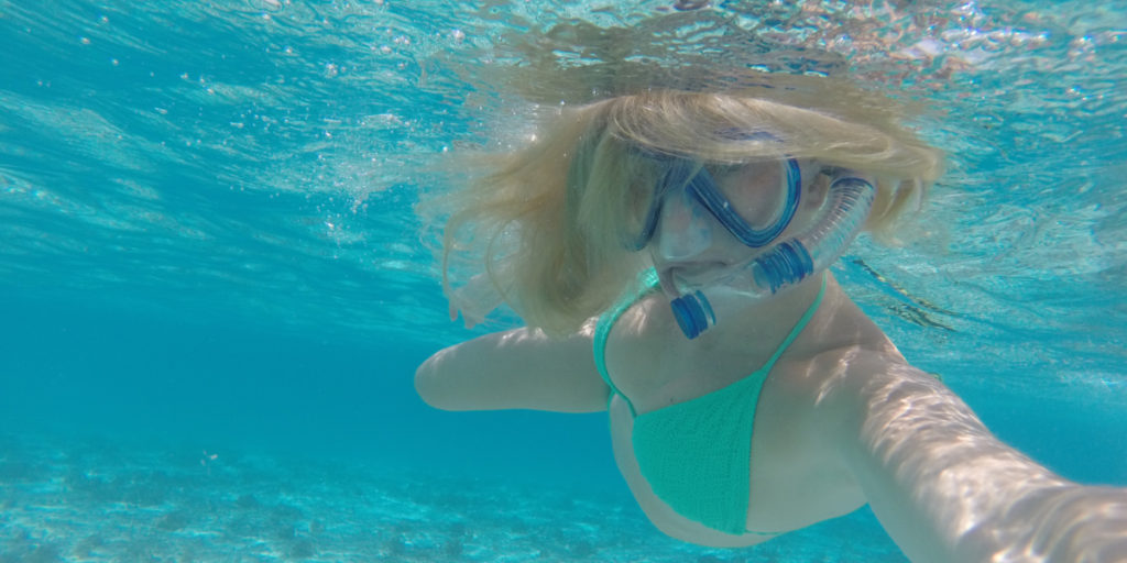 A blonde in a green bikini snorkels in the Maldives.
